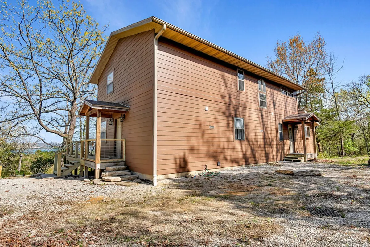 A peaceful exterior view of the wooden deck, surrounded by towering trees and featuring the home’s exterior siding. The deck offers a tranquil spot to relax, socialize, and soak in the Ozark surroundings, with easy access to both nature and the home.