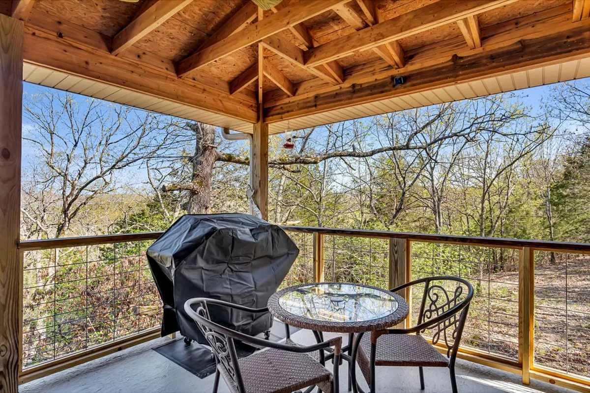 A welcoming exterior deck scene featuring a large outdoor dining table and grill, surrounded by tall trees. The setup is perfect for outdoor meals, barbecues, or simply unwinding after a day at the lake, basking in the peaceful natural setting.