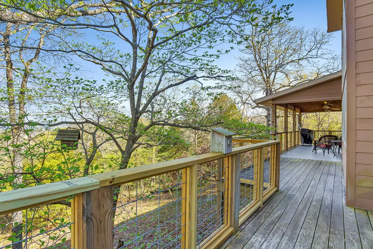 An exterior shot of a wooden deck with a railing nestled among tree canopies. There’s an outdoor seating area that looks out over the natural surroundings, ideal for relaxing, birdwatching, or winding down after lakeside adventures.