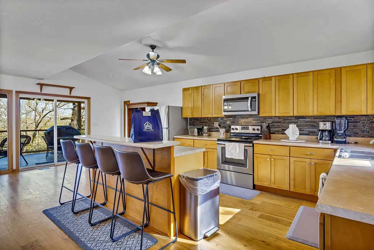 A modern kitchen equipped with a central island and bar stools, sleek stainless steel appliances, spacious countertops, and large windows that let in abundant natural light. The layout encourages group cooking and casual breakfasts while enjoying the view.