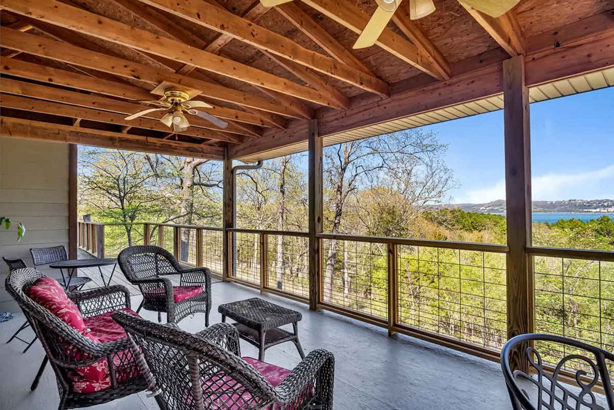 This exterior image features a cozy deck setup with wicker chairs and a wooden ceiling, offering an inviting view of the lake and surrounding landscape. The tranquil setting is perfect for morning coffee as the sun rises over the water, seamlessly blending indoor comfort with outdoor beauty.