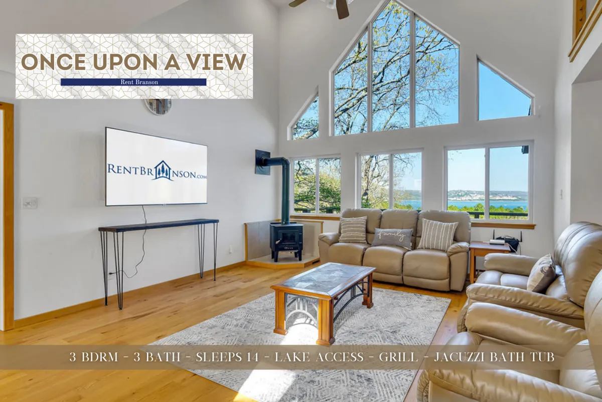 A spacious living room featuring large windows with a sweeping view of Table Rock Lake, plush leather seating, a wooden coffee table, a fireplace, and a wall-mounted television. Natural light pours in, creating a cozy and welcoming setting for family gatherings and relaxing evenings.