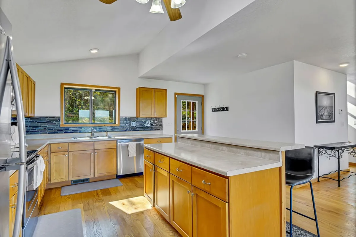 A bright, welcoming kitchen with a large island, stainless steel appliances, wood cabinetry, and a window letting in natural light. The image showcases a modern, fully-equipped kitchen perfect for preparing meals and enjoying family time.