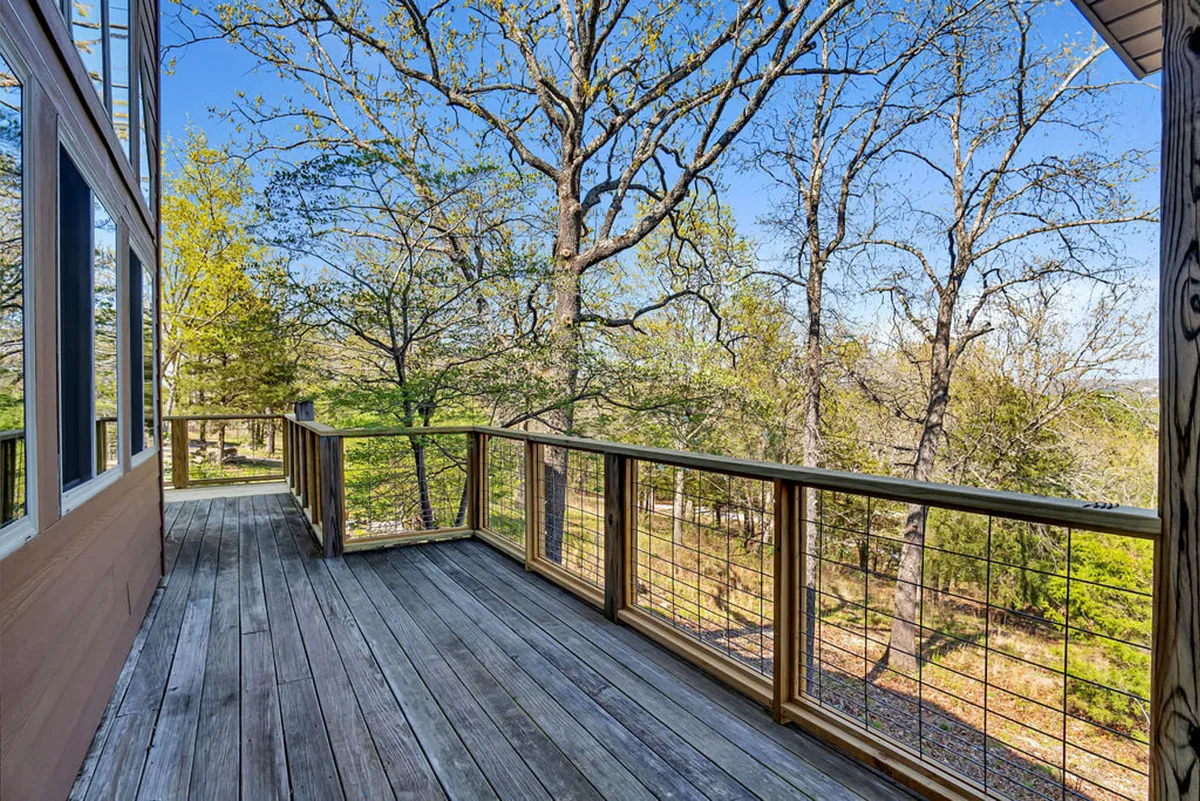 A serene wooden deck nestled among trees, with clear skies above and gentle sunlight streaming through the branches. The deck offers a perfect vantage point for sunset views and wildlife watching.