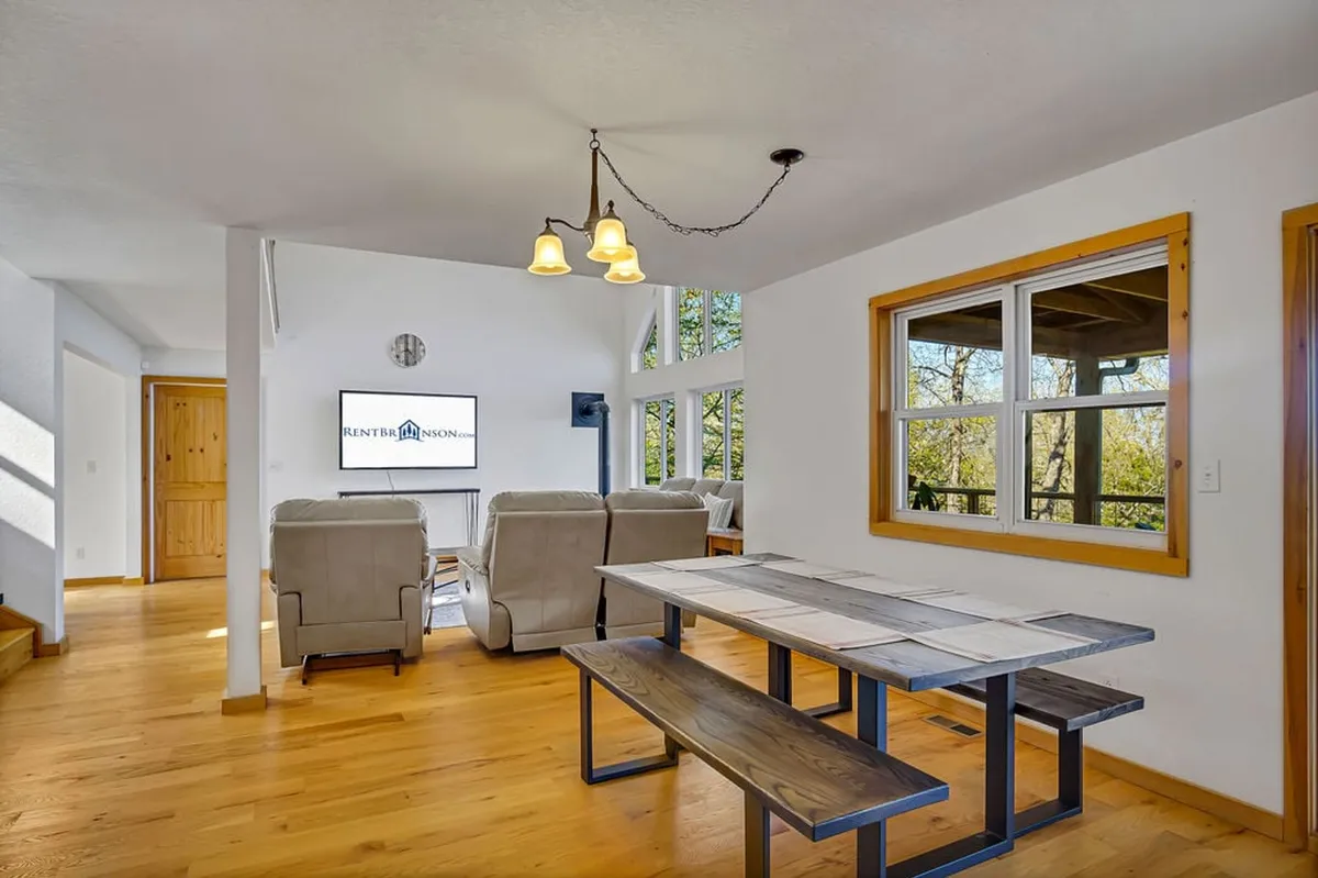 A welcoming dining area with a modern farmhouse table set near large windows, offering stunning views of the outdoors. The space seamlessly connects with a cozy seating area, radiating warmth for family meals and gatherings.