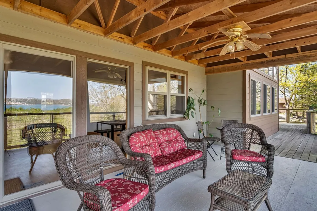 A sunlit interior space with wicker chairs, red floral cushions, a ceiling fan, and large windows looking out onto the lake. This inviting room bridges the indoor and outdoor experiences, providing a cozy spot for socializing, watching sunsets, or gathering before heading into town.