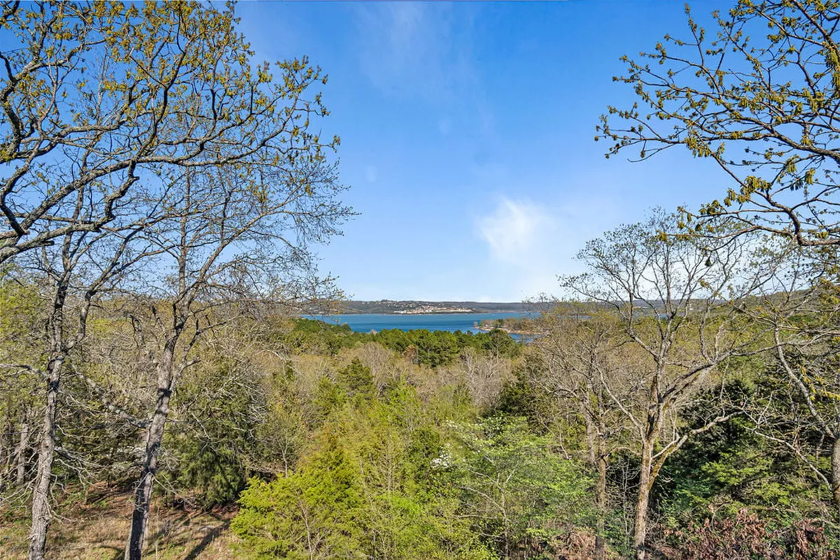 A tranquil view across a serene lake, framed by lush trees and distant rolling hills. The water glistens under soft sunlight, inviting guests to imagine mornings spent fishing or swimming, or enjoying nature’s peace.