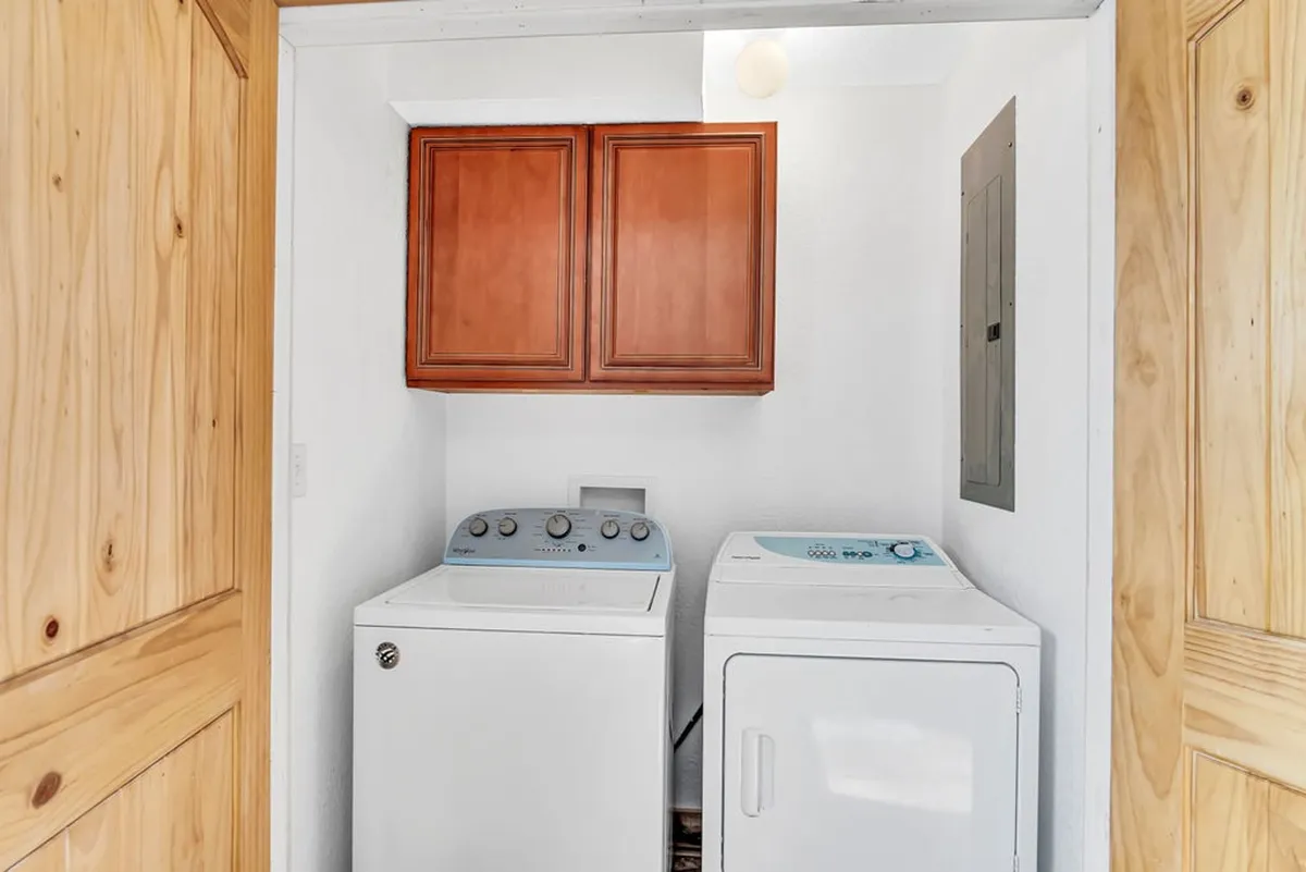 A tidy laundry area featuring a washer, dryer, and wood cabinets for organizing laundry essentials. The space is functional and well-kept, highlighting the convenience of an in-home laundry nook for guests.