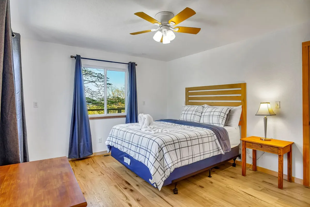 A serene bedroom with a comfortable bed, ample natural light from the window, a nightstand, and a ceiling fan. The room exudes a peaceful ambiance ideal for parents or couples seeking a restful retreat.
