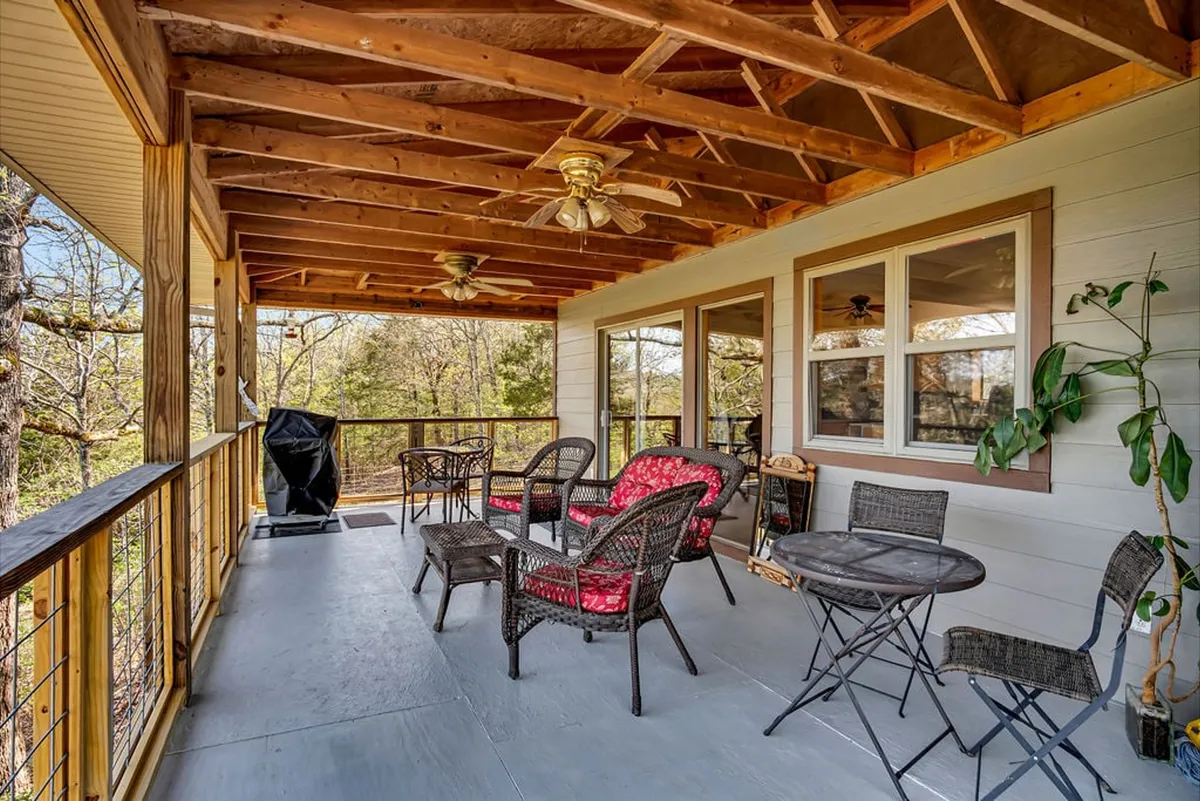 This exterior image features a comfortable outdoor seating area with wicker chairs adorned with red cushions, an outdoor table, a gas grill, and lush greenery surrounding the deck. The setting is inviting and perfect for group gatherings, meals, or relaxing moments outside, offering a direct connection to the natural environment and the lakefront atmosphere highlighted in the section.